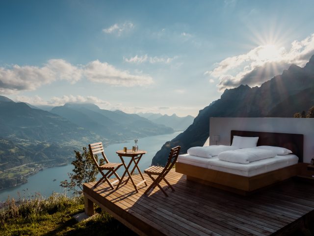 Ein Bett und Tisch und Stühle auf einer Holzplattform vor einer Bergkulisse